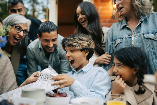 Excited boy screaming while opening his birthday gift during birthday celebration with family
