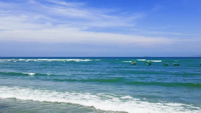 Waves crash on the shore as fishing boats bob on the water. This is Mui Ne in Lam Dong, where the ocean meets the land during the afternoon. Enjoy the natural beauty.