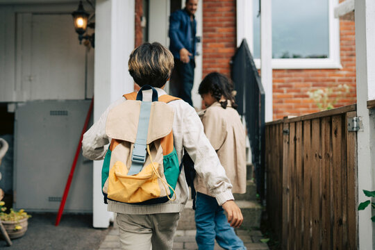 Rear view of boy and girl with backpack walking towards their house