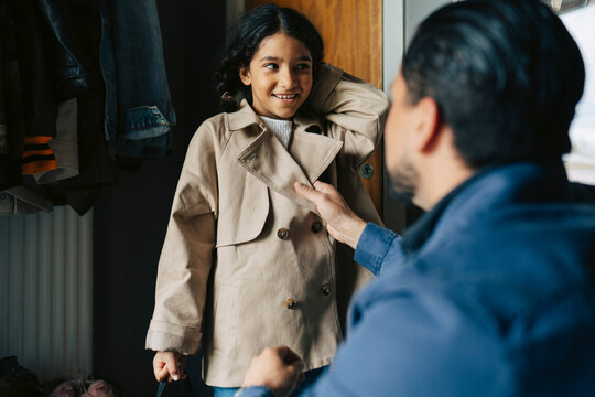 Father helping his daughter to wear jacket before leaving house