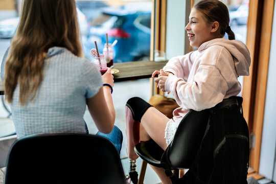 Happy girl with prosthetic leg enjoying drinks with friend while sitting in cafe