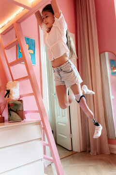 Full length of active girl with amputated leg swinging on her bunkbed in bedroom