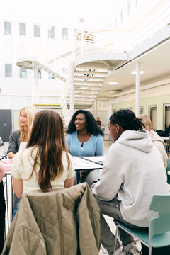 Teenage students discussing about project while sitting at table in secondary school