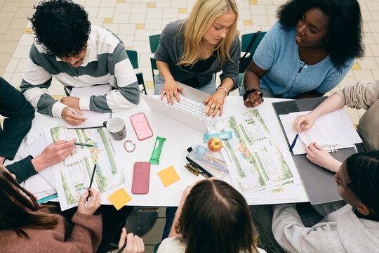 High angle view of college students making notes for sustainability project presentation while sitting at table