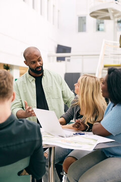 Male professor sharing ideas with female students making project in college