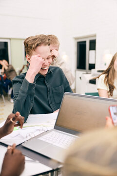 Happy teenage boy making project with classmates in high school
