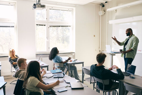 Mature male professor explaining mathematical formula to teenage students in classroom at high school