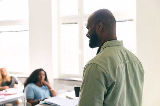 Smiling male teacher with shaved head teaching in high school classroom