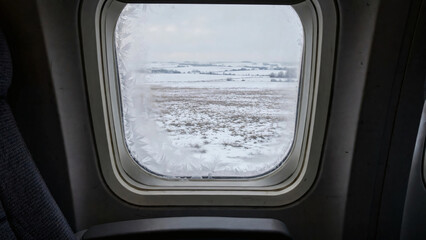 Obraz premium Frosted airplane window over snowy landscape