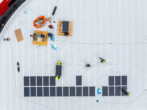 Aerial view of workers installing solar panels on a marine fish farming pen with white surface and equipment in Liabygda, More og Romsdal, Norway.