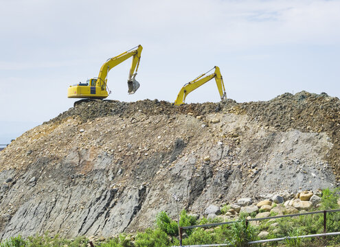 Aerial view of two yellow excavators working on a large pile of dirt and gravel at a construction aggregate plant in Taiwan.