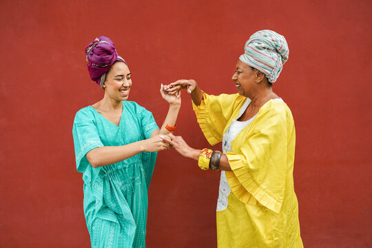 Happy african mother and daughter dancing together while wearing traditional clothes - Motherhood, music, ethnic cultures and family concept - Focus on faces - UGC content