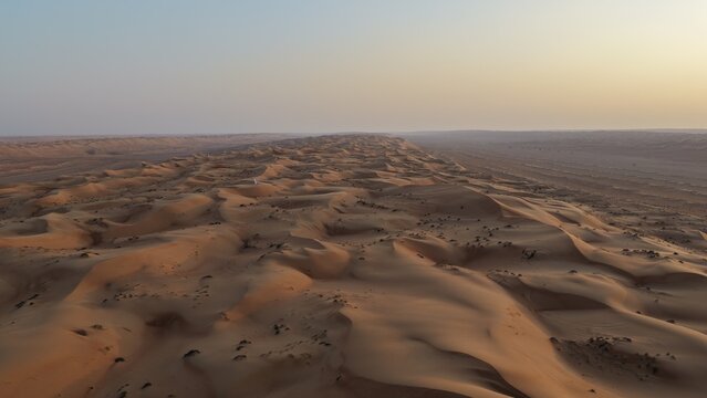 Aerial view of the vast sand dunes of Wahiba Sands at sunset, with golden light casting long shadows across the desert landscape in Muscat, Muscat Governorate, Oman.