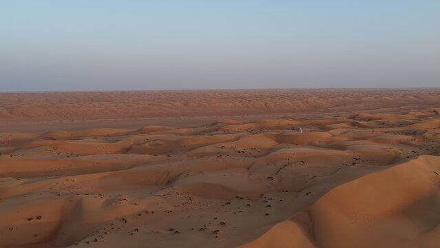 Aerial view of the vast dunes of Wahiba Sands, showcasing the undulating golden sand landscape under a clear sky in Muscat, Muscat Governorate, Oman.