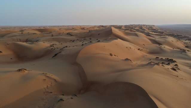 Aerial view of vast undulating sand dunes of the Wahiba Sands desert under a clear sky in Muscat, Muscat Governorate, Oman.