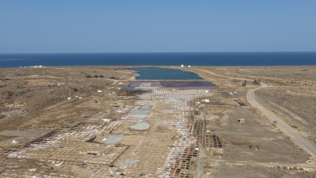 Aerial view of the salt pans in Qurayyat, featuring rectangular evaporation ponds, arid landscape, and the coastline of the Arabian Sea. Qurayyat, Muscat Governorate, Oman.