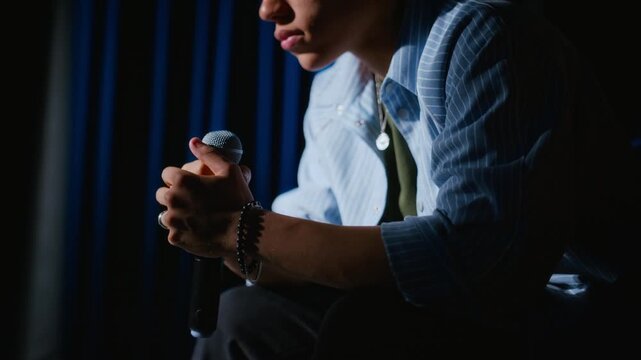 Young actor sitting backstage holding microphone tightly while preparing for stage performance. Footage suitable for public speaking coaching, theater education, and stage fright campaigns