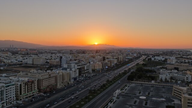 Aerial view of Muscat at sunset with golden light illuminating the cityscape, modern buildings, and a busy highway in Muscat, Muscat Governorate, Oman.