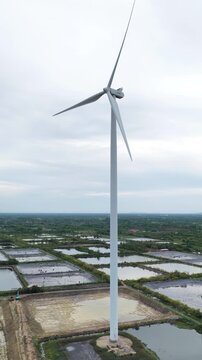 An aerial view of wind turbines for electricity generation near the sea with shrimp ponds and farmland below captured by a drone camera.