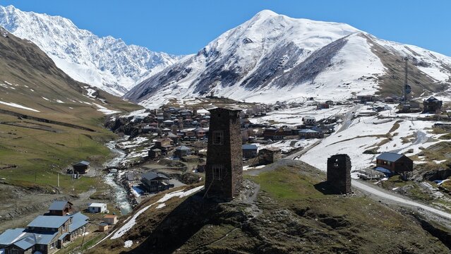 Aerial view of historic Ushguli village with Svan defensive towers, nestled in a valley surrounded by snow-capped Caucasus mountains and a river in Ushguli, Samegrelo-Zemo Svanet, Georgia.
