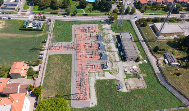 Aerial view of C.P. Seguro electrical substation with high-voltage power lines, transformers, and switchgear equipment in a fenced area in Settimo Milanese, Lombardy, Italy.