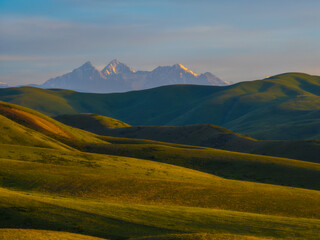 Fototapeta premium Golden Hour Over Rolling Hills and Snow-Capped Mountains