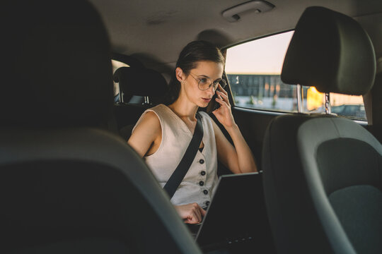 Businesswoman talking on a smartphone while using a laptop in the back seat