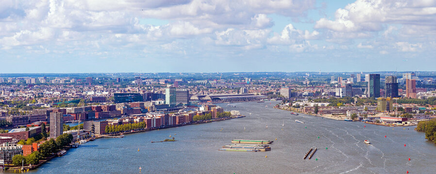 Aerial view of the IJ river in Amsterdam, featuring the modern skyline, busy waterways with cargo barges, and historic urban architecture in Amsterdam, North Holland, Netherlands.