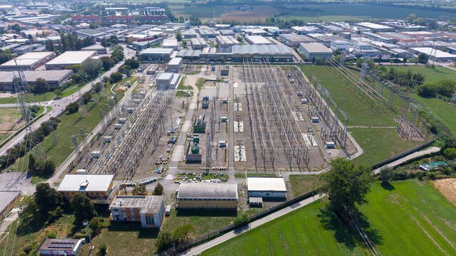 Aerial view of the Terna Baggio electrical substation featuring high-voltage power lines, transformers, and industrial infrastructure surrounded by green fields in Settimo Milanese, Lombardia, Italy.