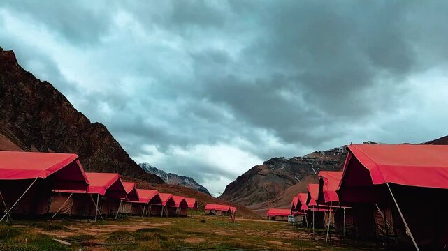 Red glamping tents arranged in rows across a green mountain valley under dark stormy clouds during a remote outdoor adventure in the wilderness