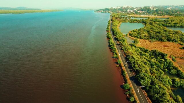 Expansive aerial view showcasing a tranquil river winding gracefully alongside a scenic road, enveloped by lush green trees and distant coastal elements