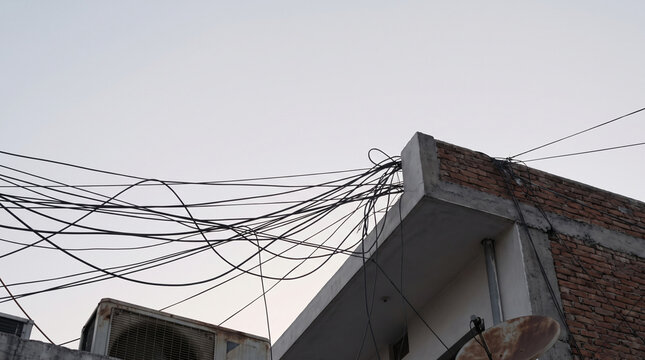 Tangled electric wire cables overhead on old building rooftop seen against clear sky