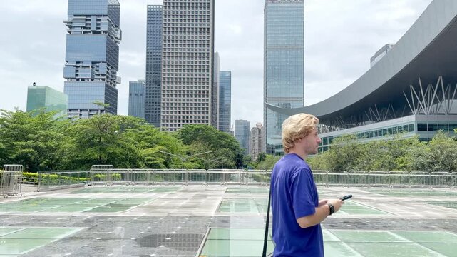 Young Man Scrolling and Photographing with Phone at Shenzhen Square
