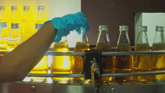 Quality control worker inspecting sealed beverage bottles on an automated conveyor belt in a modern industrial plant, ensuring hygiene, packaging integrity, and food safety standards.