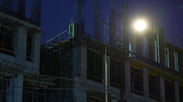 Construction workers assembling formwork components on the upper level of an unfinished concrete building. Active structural construction process preparing the framework for further concrete work and 