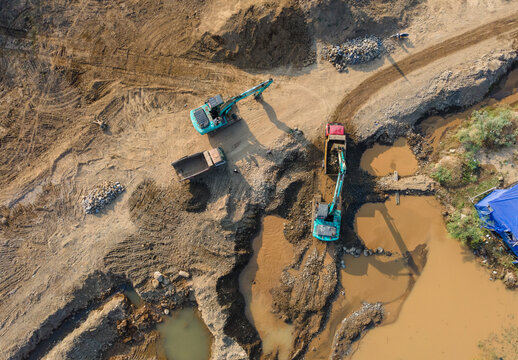 Aerial view of excavators and dump trucks working on a muddy construction site with pools of water in Karanglewas, Central Java, Indonesia.