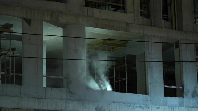 Construction worker using an angle grinder during active work inside an unfinished multistory building. Industrial construction process showing power tool operation, structural work 