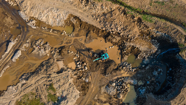 Aerial view of an excavator working in a muddy excavation site with piles of rocks and earth in Karanglewas, Central Java, Indonesia.