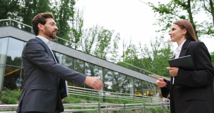 Businessman and businesswoman meeting, shaking hands and negotiating a business deal, outdoors