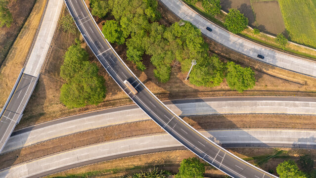 Aerial view of a highway interchange with a truck driving on the road, surrounded by lush green trees and agricultural fields in Boyolali, Central Java, Indonesia.