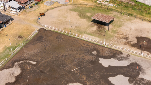 Aerial view of a horse in a dirt riding arena with a small shelter and white fencing in Yogyakarta, Special Region of Yog, Indonesia.