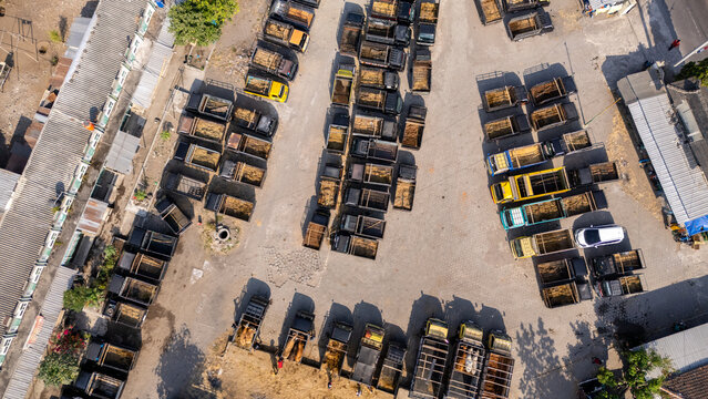 Aerial view of a large parking lot filled with numerous dump trucks and commercial vehicles arranged in rows on a dusty ground in Yogyakarta, Special Region of Yogyakarta, Indonesia.