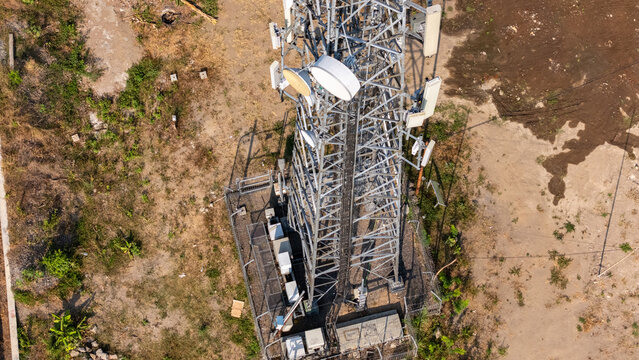 Aerial view of a telecommunications tower with antennas and equipment cabinets in a fenced area surrounded by dry ground in Yogyakarta, Special Region of Yogyakarta, Indonesia.