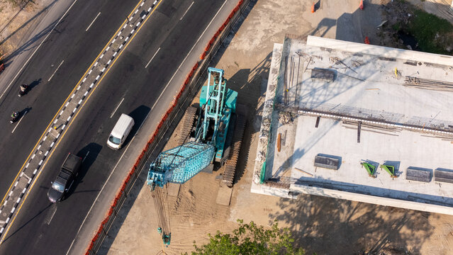 Aerial view of a construction site with a large blue crane, concrete structures, and a nearby road with traffic, Yogyakarta, Special Region of Yog, Indonesia.