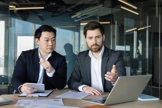 Two diverse businessmen in formal wear discussing strategy, analyzing data, and collaborating on a new project during a professional meeting in a modern office