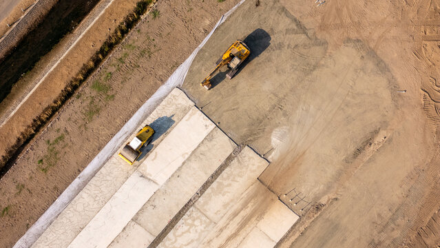 Aerial view of an excavator and a road roller working on a construction site with concrete sections and dirt ground in Yogyakarta, Special Region of Yog, Indonesia.