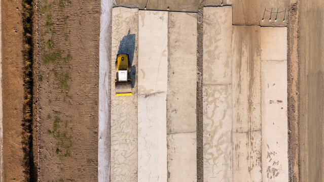 Aerial view of a yellow road roller compacting concrete slabs at a construction site in Yogyakarta, Special Region of Yogyakarta, Indonesia.