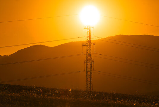 Aerial view of an electricity pylon silhouetted against a vibrant sunset with rolling mountains in the background in Cerin, Banska Bystrica Region, Slovakia.