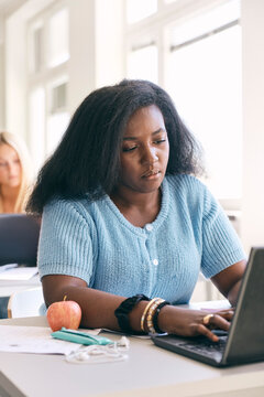 High school female student studying on laptop while sitting at desk in classroom