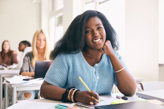 Portrait of smiling secondary female student sitting at classroom desk in school